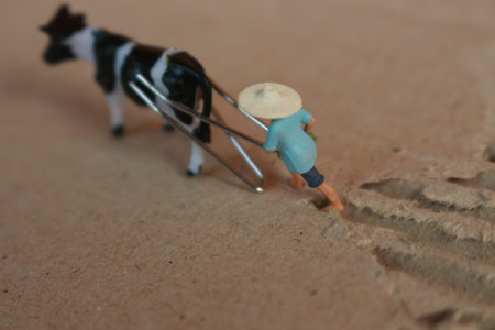miniature figure of a farmer plowing a field with his cow on a cardboard.の写真素材