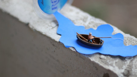 a miniature figure of a fisherman fishing in a river visualized on blue paper cutouts.の写真素材
