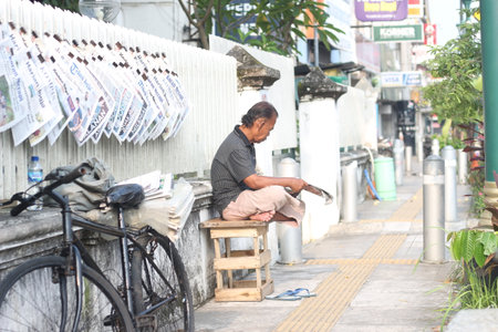 Yogyakarta, Indonesia - March, 19 2023. an old man reading a newspaper on the side of the road.のeditorial素材