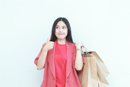 portrait of beautiful asian woman wearing red outfit gesturing carrying lots of shopping bags with happy expression isolated on white background.の写真素材