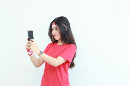 portrait of beautiful asian woman wearing red outfit celebrating Indonesia independence day looking at mobile phone with happy expression isolated on white background.の写真素材