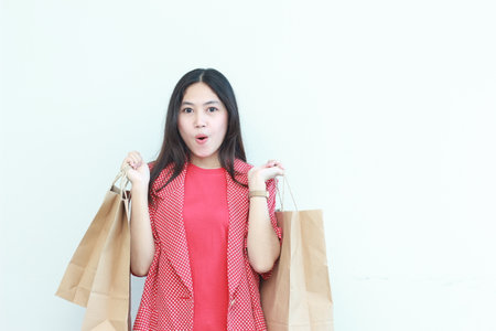 portrait of beautiful asian woman wearing red outfit gesturing carrying lots of shopping bags with surprised expression isolated on white background.の写真素材