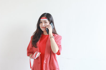 portrait of beautiful asian woman wearing red outfit celebrating Indonesia independence day while calling with smiling expression isolated on white background.の写真素材