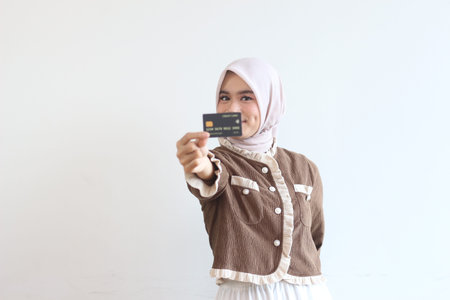 A smiling young woman in a hijab holds up a credit card. Online shopping concept.