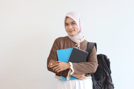 A cheerful young Muslim student, carrying her books and backpack, smiles confidently.  Ready for class.の写真素材