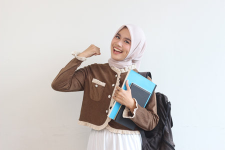 A smiling young Muslim woman confidently holds her books and backpack, ready for class.  She embodies academic success and determination.の写真素材