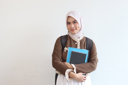A cheerful young Muslim student girl holding her books and backpack smiles at the camera.の写真素材