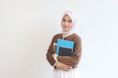A smiling young Muslim woman in a hijab holds books, representing education and success.  She exudes confidence and hope.の写真素材
