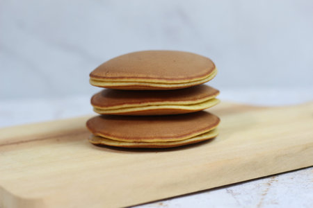 A tempting stack of three fluffy Japanese pancakes sits on a light wooden board. The pancakes have a...