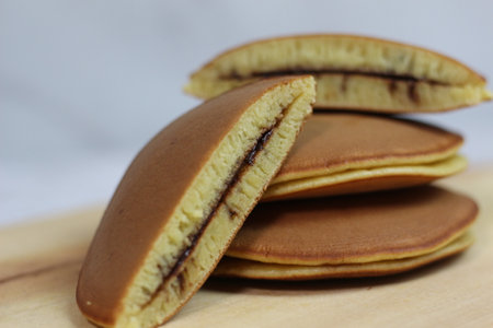 A stack of dorayaki pancakes filled with chocolate, beautifully arranged on a wooden board. The warm brown color and inviting texture are enticing.の写真素材