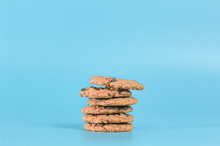 Close-up of several chocolate chip cookies stacked on a blue background.