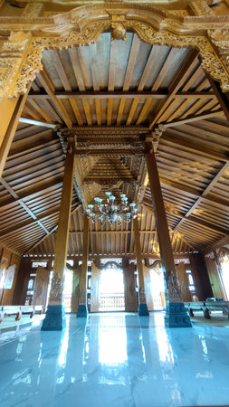 Interior view of a traditional wooden pavilion featuring intricate carvings, a central chandelier, and natural light creating a warm, elegant atmosphere, ideal for cultural or wedding events.の写真素材