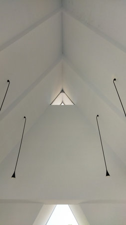 A minimalist white ceiling with a triangular skylight and four hanging lights creating a clean, airy, and sophisticated atmosphere ideal for modern architectural design and interior decor.の写真素材