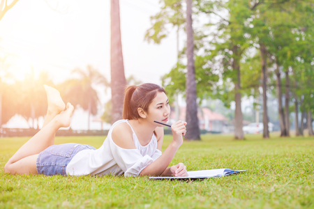 the women is on the grass and beautiful. She is thinking. the book is on the grass. she wear white dress.の写真素材