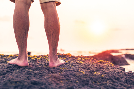 the man stand on the rock between beach and sunset. he wear brown pantsの写真素材