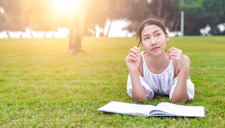 the women is on the grass and beautiful. She is thinking. the book is on the grass. she wear white dress.の写真素材