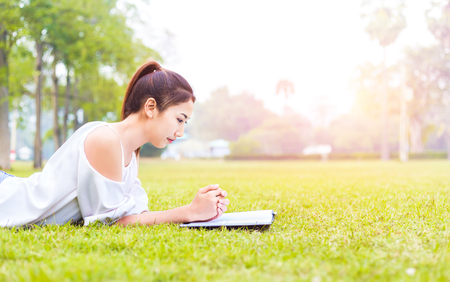 the women is on the grass and beautiful. She is thinking. the book is on the grass. she wear white dress.の写真素材