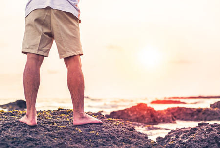 the man stand on the rock between beach and sunset. he wear brown pantsの写真素材