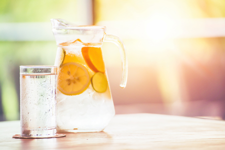 the fruit in the water and ice is on the table. the water in glass near jar.の写真素材
