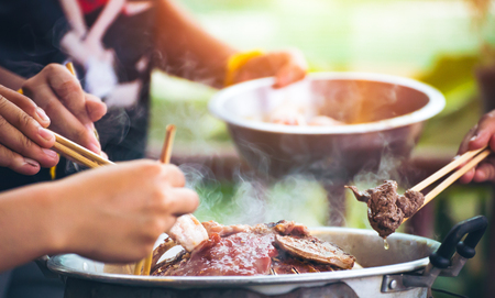 People cooking meat and grill. Food are vegeteble. People use chopsticks.の写真素材