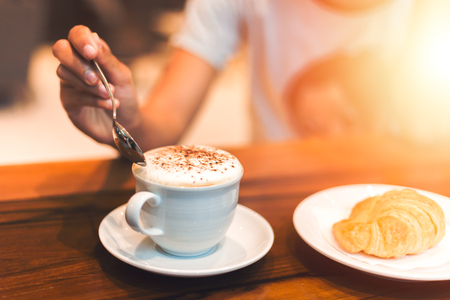 hands hold a cup of coffee and spoon in the dish.の写真素材