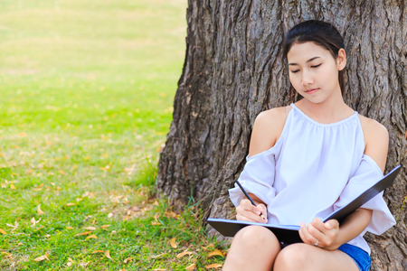 Women sitting near big tree and drawing in the park.の写真素材
