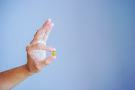 Close up photo of one round yellow pill in hand. Man takes medicines with glass of water. Daily norm of vitamins, effective drugs, modern pharmacy for body and mental health.の写真素材