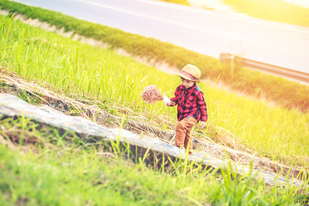 a children wear hat and walking on stair. A children hold flower and near the road.の写真素材