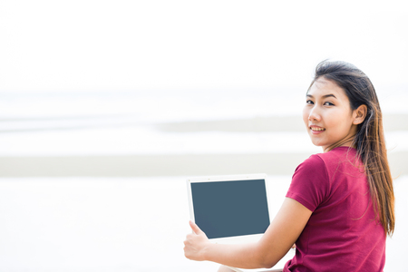 Women is smile and hold computer near the beach.の写真素材