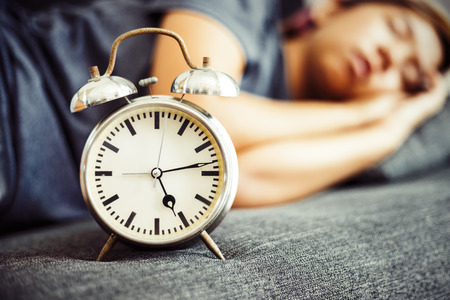 A clock is on the bed near women sleeping.の写真素材