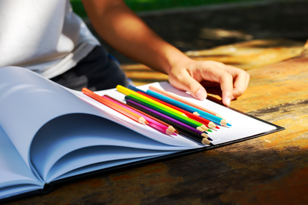 Student hand is on the wood table.The crayon is on the white paper.の写真素材