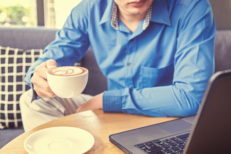 Businessman hold cup of coffee. A cup of coffee is on the table near the laptop.の写真素材