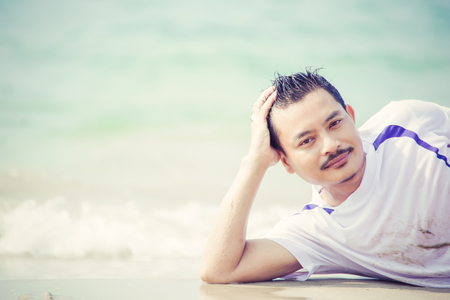 Asian man laying on the beach and water flow in the summer time.の写真素材