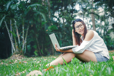 the women sitting on the wood box and working with notebook. She working in the park.の写真素材