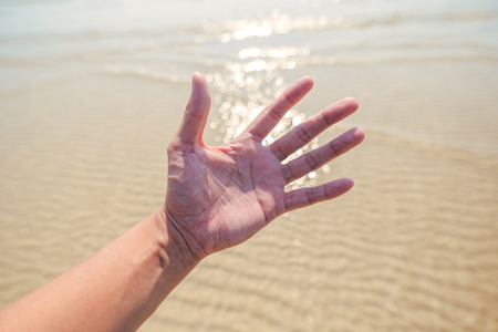 Hand of a man reaching to towards beach. Hand make symbol.の写真素材