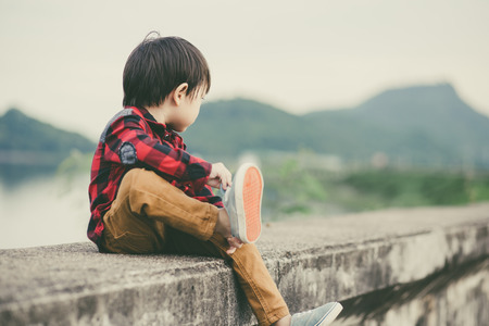 A lonely children take off the shoes and he is sitting on the groundの写真素材
