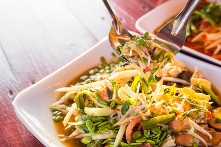 hand of women scoop up the Spicy papaya salad called "Somtum" in Thai on wooden table with sunlight ray.の写真素材