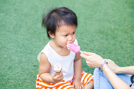 asian child and mom eating ice-cream together in the parkの写真素材