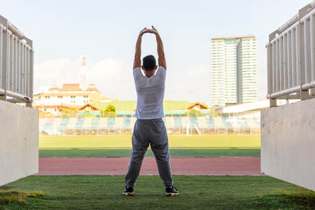 Full length portrait of a athletic man stretching in the morning and standing at sport stadium.の写真素材