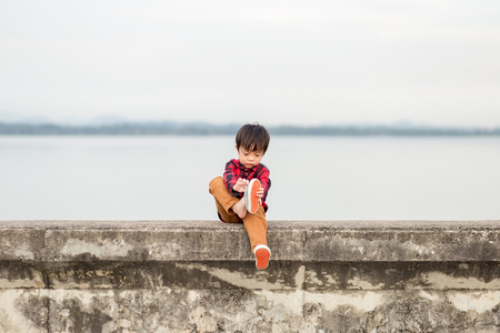 A lonely children take off the shoes and he is sitting on the groundの写真素材