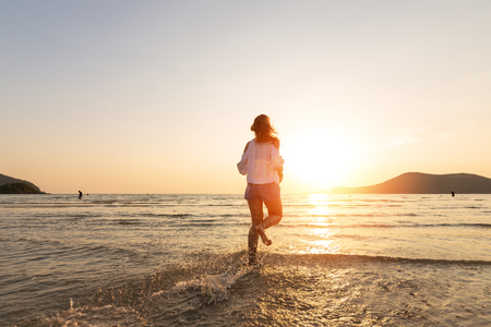 A woman running in to the beach. Woman happy with vacation summer on the beach and sunset.の写真素材