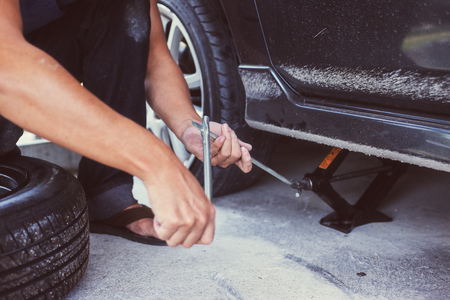 Hands using hydraulic jack - car maintenance concept. Car tire changed for maintenance in garageの写真素材