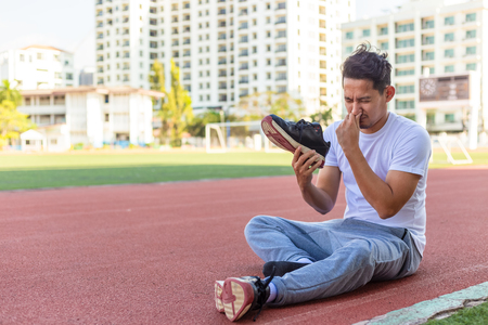 a man disgusted by the smell of his running shoe. A sport man sitting on the  track race at stadium.の写真素材