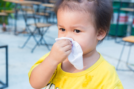 little child girl wiping and cleaning nose with tissue on her handの写真素材