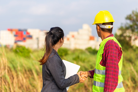 Businesswomen and foreman shake hands together. Engineer and manager teamwork and checking at site construction .の写真素材