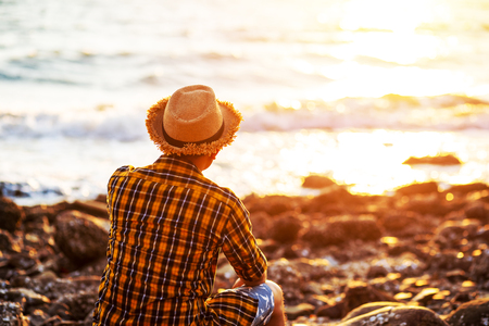 A man travel and  sitting on the stone near sea water and sunset in summer.の写真素材