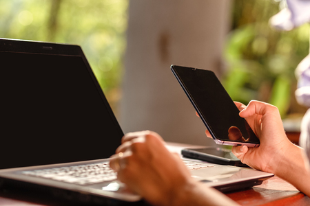 women use phone and working in laptop in the park. the laptop is on the table.の写真素材