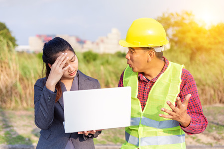 Men in hard hats and uniform with young woman. Team of architects, engineers discussing work. A women hold laptop.の写真素材