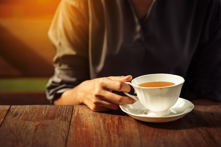 Woman's hands holding white cup of tea or coffee on sun light. Morning time for breakfastの写真素材