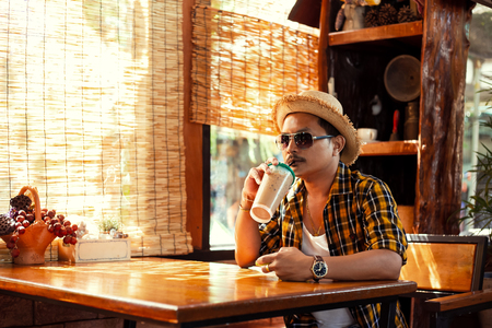 A man wear sunglasses and hat and drink ice coffee at summer.の写真素材